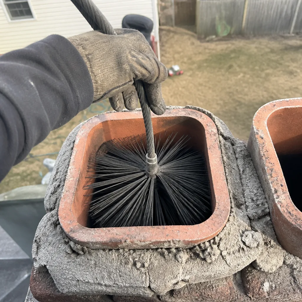 Professional chimney sweep cleaning a brick chimney flue with a wire brush